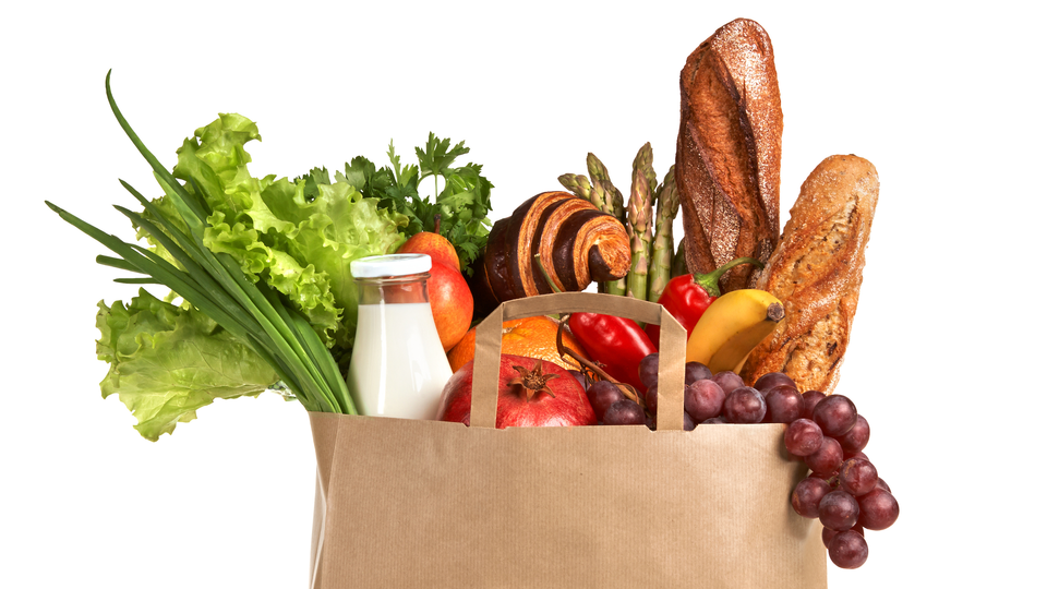A brown shopping bag where vegetables, bread and other groceries can be seen