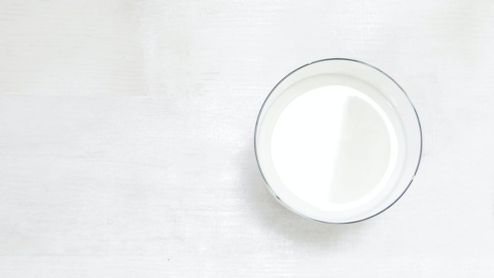 Photo from above of a glass of milk standing on a white table.