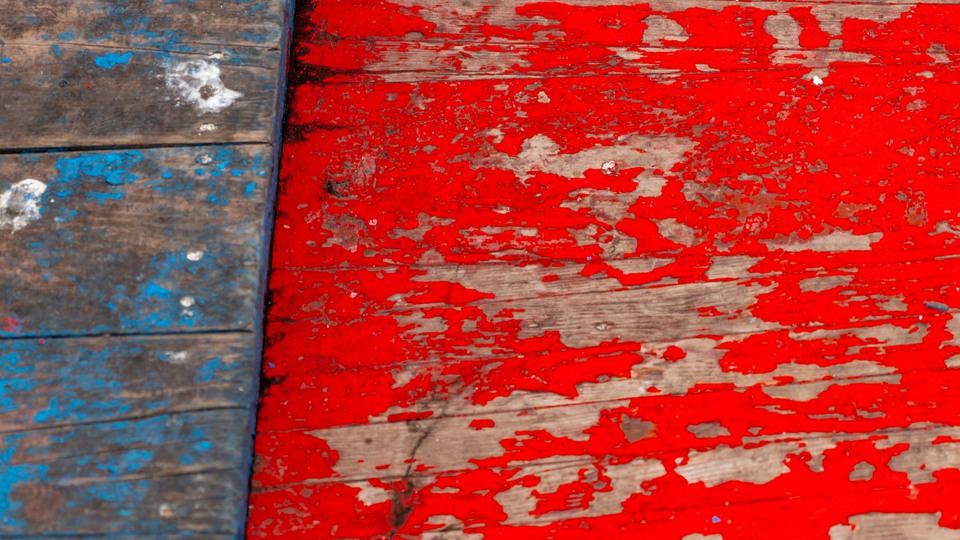 Wooden planks in blue and red which are heavily weathered. The colour peels off strongly. The wood can be seen under the paint.