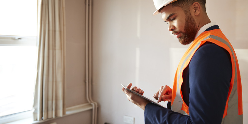 Surveyor In Hard Hat And High Visibility Vest holding a Digital Tablet, Preforming a House Inspection