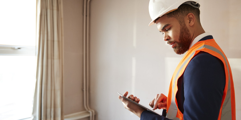 Surveyor In Hard Hat And High Visibility Vest holding a Digital Tablet, Preforming a House Inspection