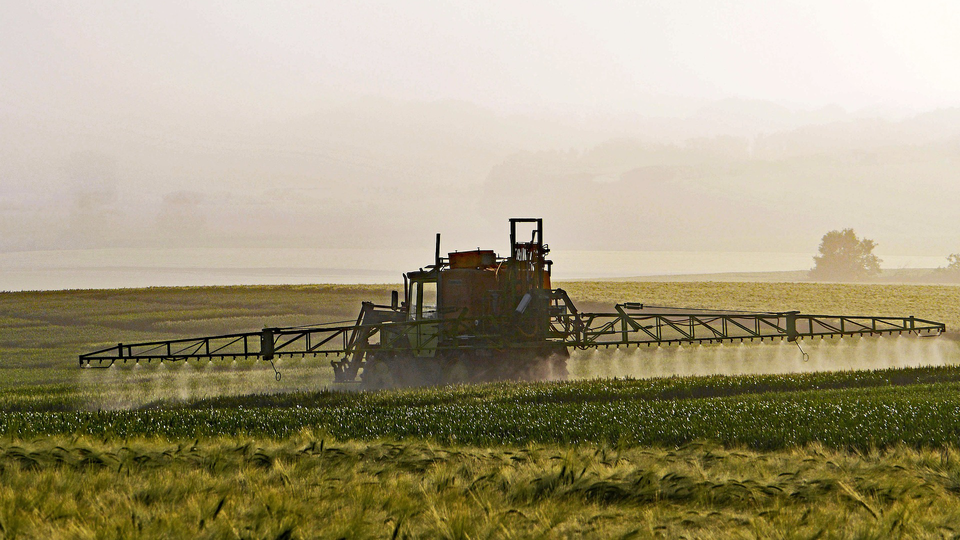 A tractor on a field, spreading pesticides.