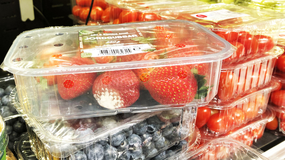 En plastförpackning med jordgubbar varav en av jordgubbarna är dålig. 