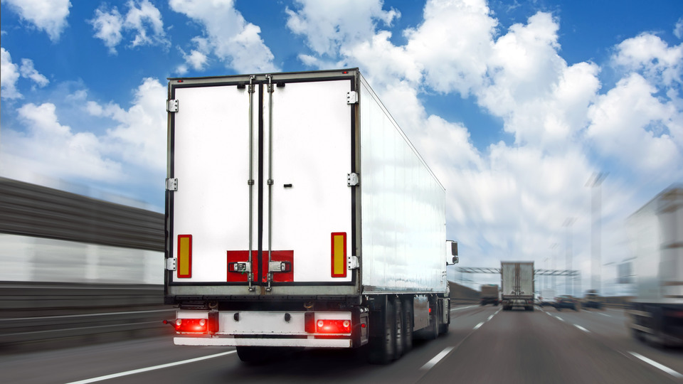 Truck with a white trailer drives motion blur effect speed along the highway in heavy traffic in the with clouds in the sky