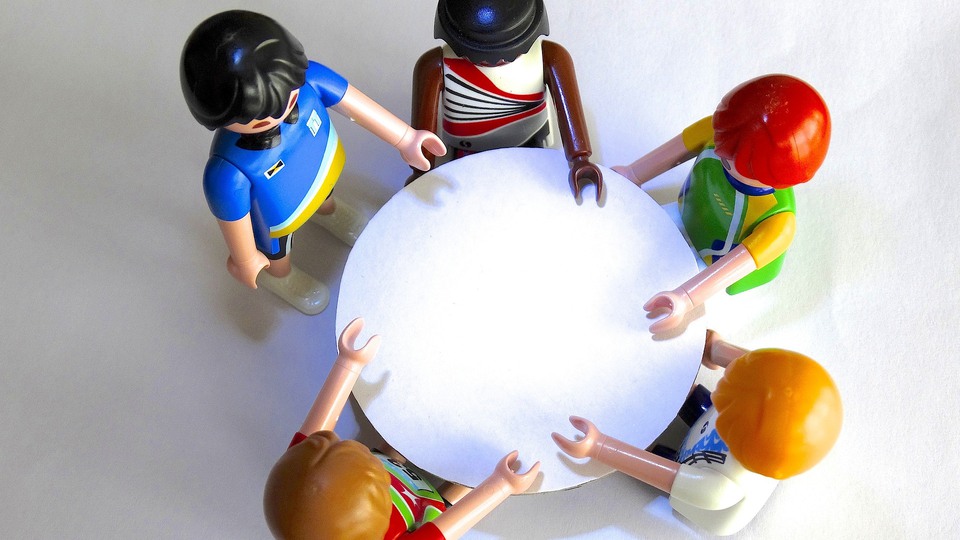 Fem plastfigurer från leksaktillverkaren Playmobil står runt ett bord, fotograferade uppifrån.