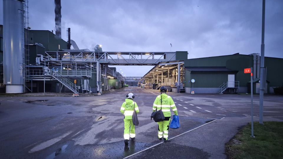 Två personer i skyddskläder går mot en anläggning
