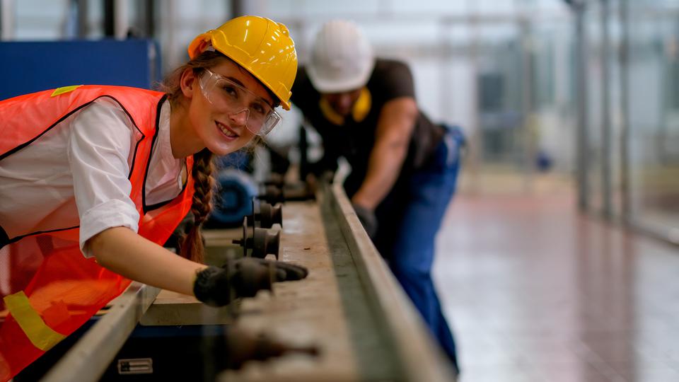 Worker or technician or engineer woman smile and look forward in front of rail of the machine with her co-worker as background in factory.