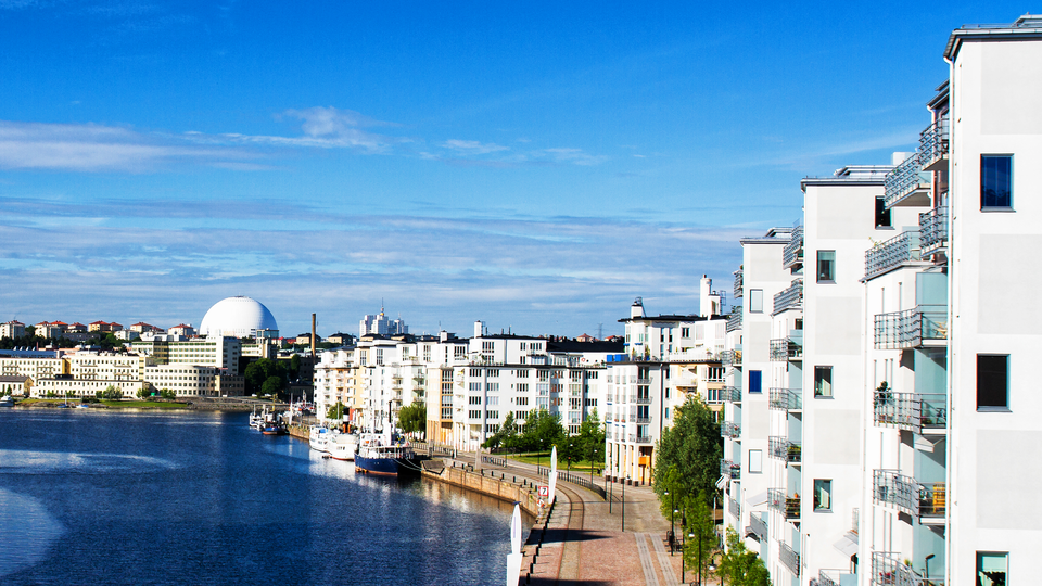 New and modern settlement in Stockholm, Sweden.  Big white apartment complex right by the water, a view of Globen in the distance.