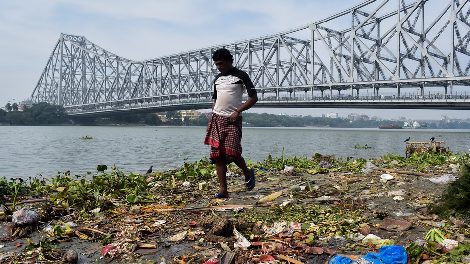 Man går vid nedskräpad flod i Indien