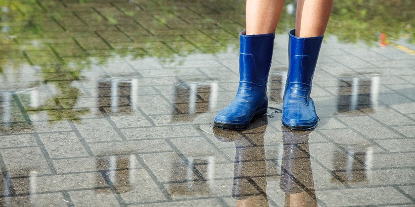 girl in rubber boots standing in a puddle after a rain outdoor on summer day. legs closeup