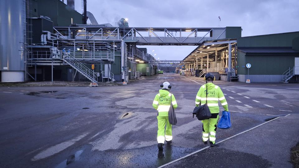 Två personer i skyddskläder går mot en anläggning