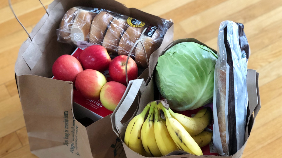 Två papperkassar med matvaror: äpplen, bananer, vitkål och bröd.