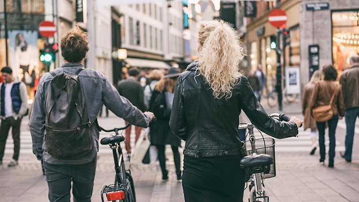 Couple walking with city bikes in Copenhagen street shopping. Urban living lifestyle. Commuting with bicycle, young students couple tourists traveling in Europe.